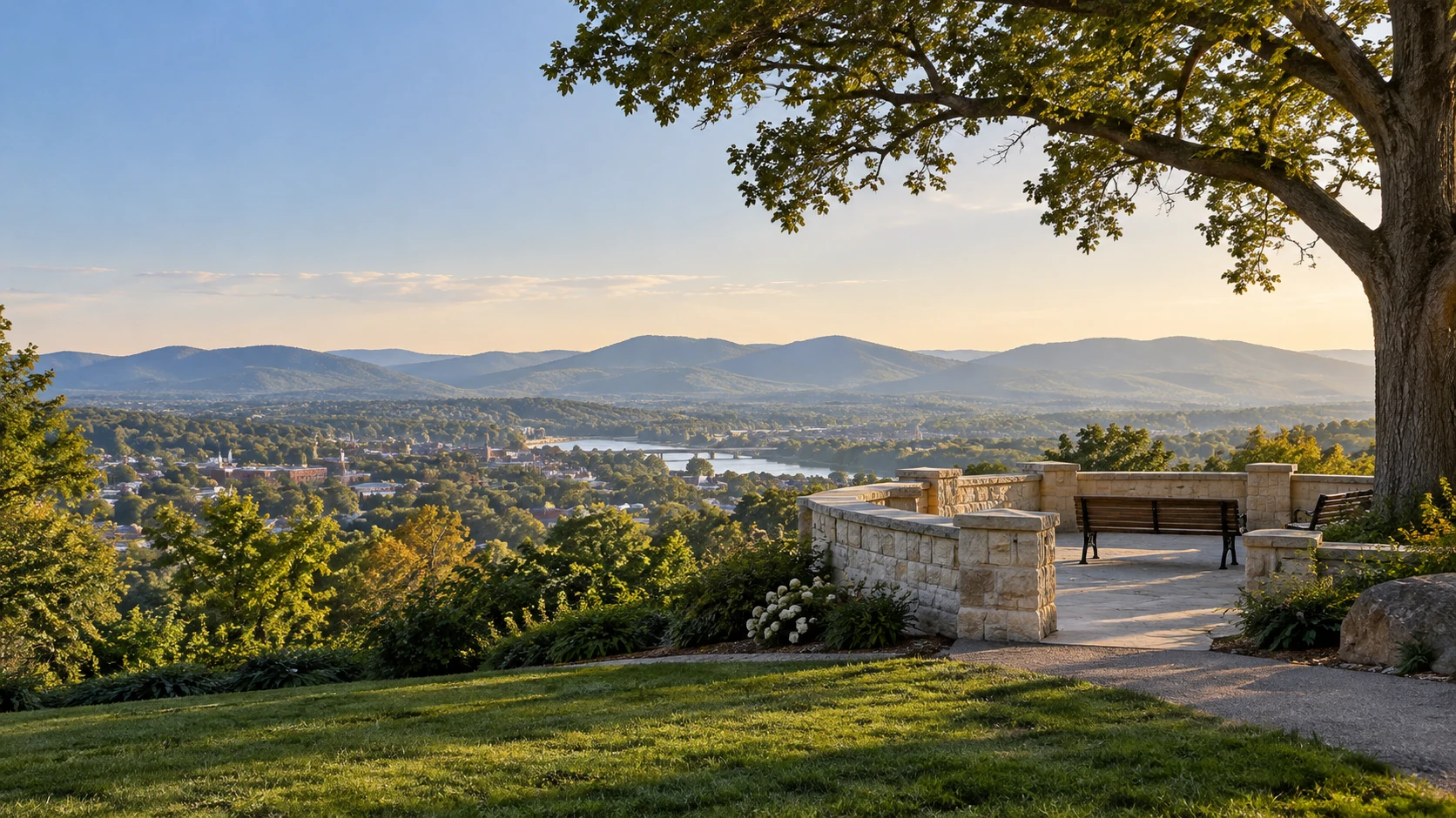 A tree-lined park overlook with a wider view of a town and distant hills.
